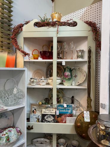 Antique cabinet filled with vintage glassware, ceramics, and cookbooks.