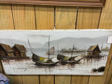 Painting of traditional boats and houses on stilts over water with mountains in the background.