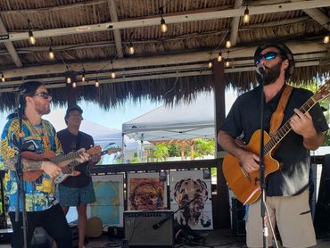 A band performs live on a wooden stage under a thatched roof.