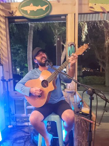 Man playing guitar and singing at a cozy outdoor venue at night.