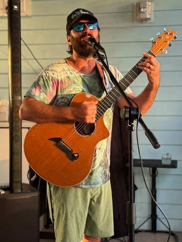 Man playing acoustic guitar and singing into microphone indoors.