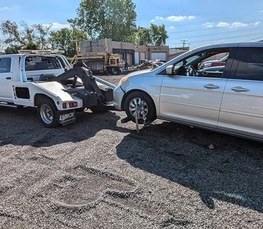 Tow truck accidentally damages a white van's front while hooking it up.
