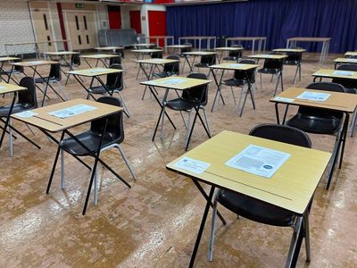 Empty classroom with spaced desks and exam papers.