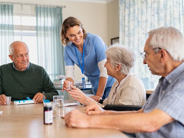 Caregiver assisting seniors with medication at table.