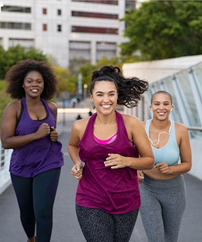 Three women jogging outdoors and smiling.