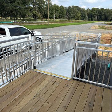 Metal wheelchair ramp with wooden deck outside a building near a white pickup truck.