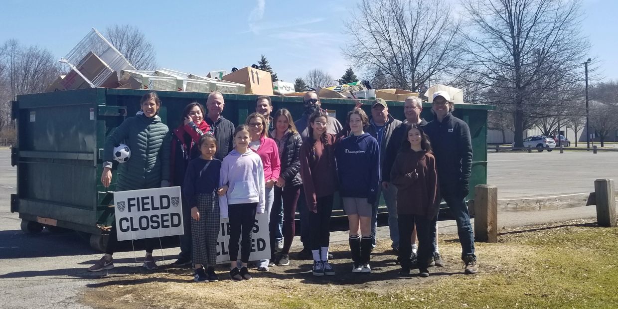 Group of people standing by a trash-filled dumpster with 'Field Closed' signs.