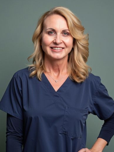 Smiling woman in navy blue medical scrubs against a gray background.