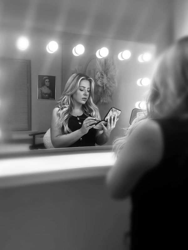 Woman applying makeup in front of a mirror.