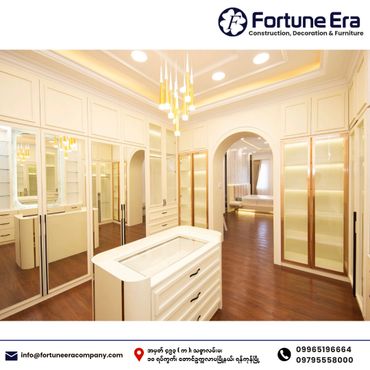 Luxurious walk-in closet with white cabinetry and warm wooden flooring.