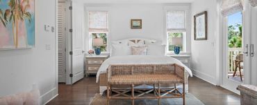 Bright and airy bedroom with white walls, wooden flooring, and cozy wicker bench.