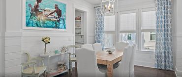 Bright dining room with white chairs, a wooden table, and blue patterned curtains.