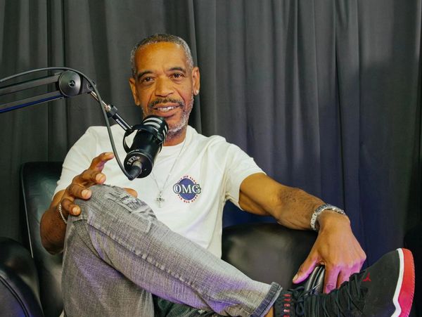 Man sitting in a chair speaking into a microphone with relaxed posture.