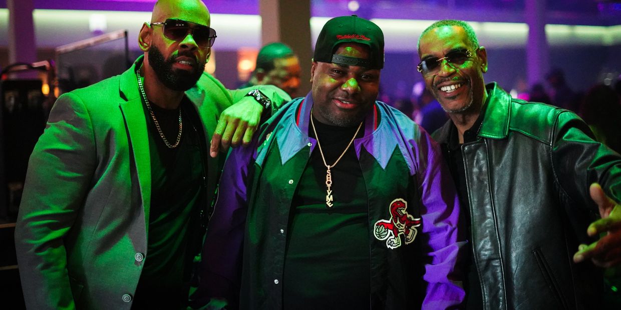 Three men posing together in a lively, colorful nightlife setting.