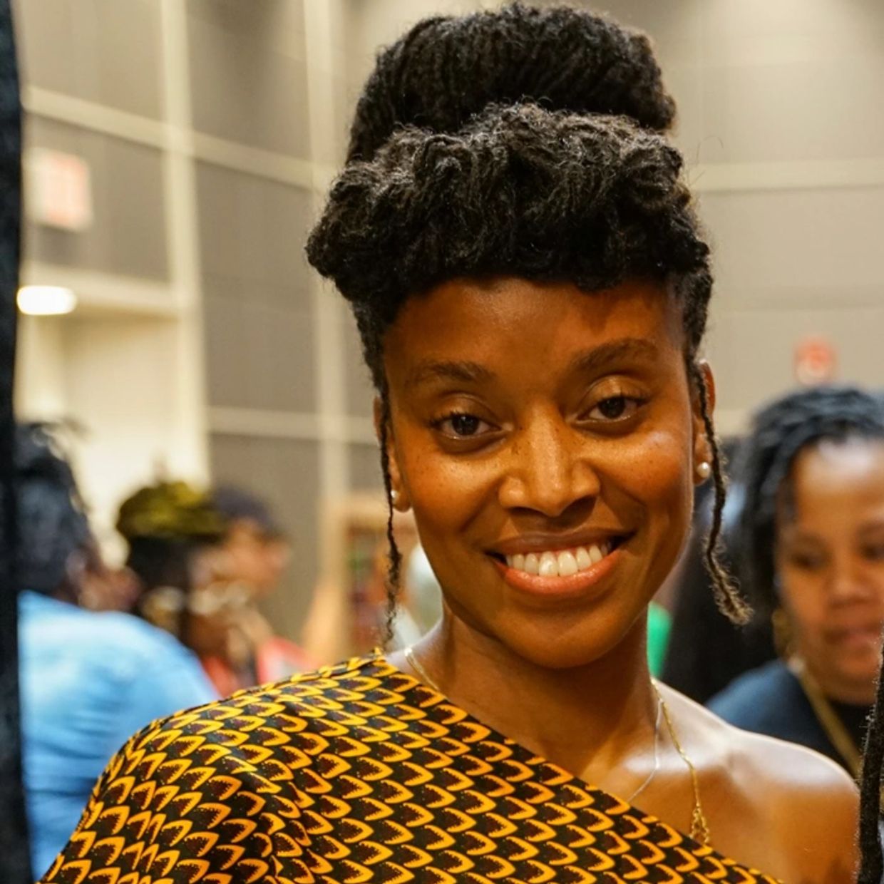 Smiling woman with natural hair and African-patterned clothing.