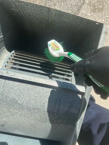 Hand cleaning a metal vent with a brush.