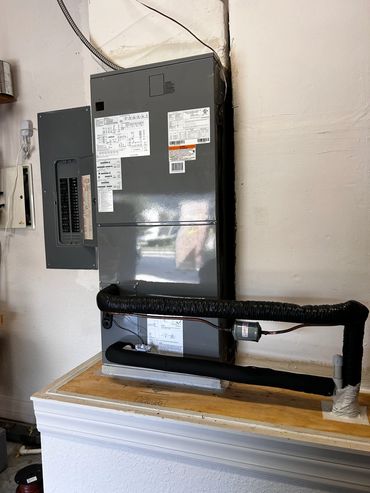 Gray HVAC unit with insulated pipes mounted indoors.