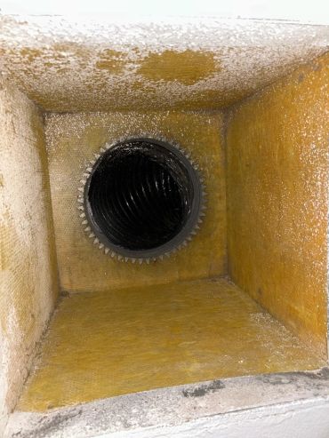 Interior of a dirty HVAC duct with a black vent pipe.