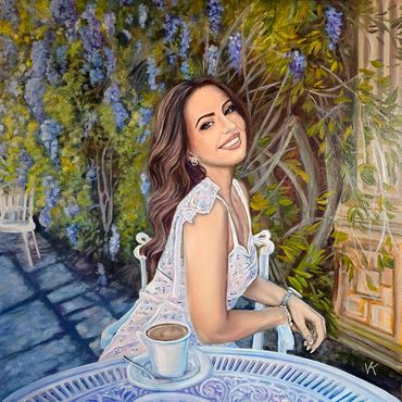 A smiling woman in a floral dress sits at a table with coffee, surrounded by lush greenery and flowers.