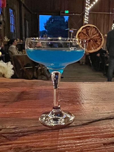Blue cocktail in a coupe glass garnished with a dried citrus slice on a wooden table.