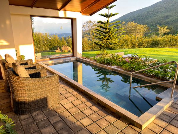 Cozy patio with wicker chairs and a small pool overlooking a green landscape and mountains.