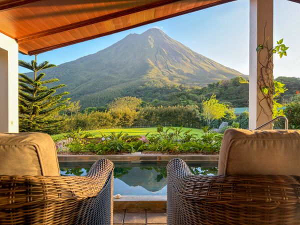 Cozy wicker chairs overlook a serene mountain and lush garden view.