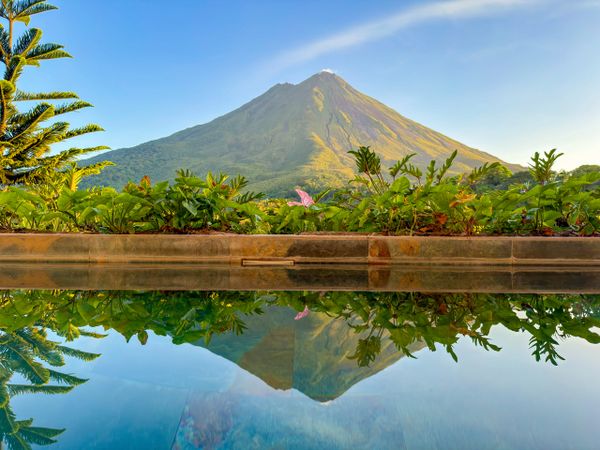 A clear mountain reflected in a calm pool with surrounding greenery.