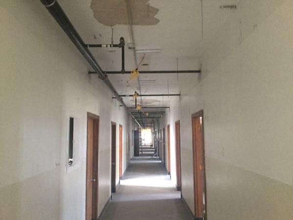 Long, empty corridor with multiple doors and exposed ceiling pipes.