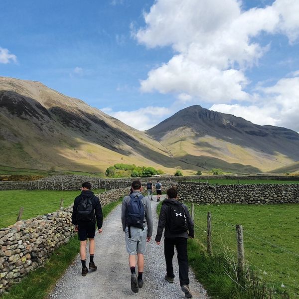 Three hikers walking on a gravel path with mountains and blue sky in the background.