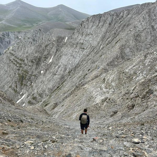 A hiker with a backpack walks through a rugged mountainous terrain.