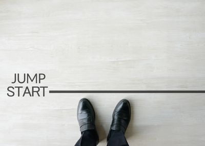 Person in black shoes standing near line with words 'JUMP START'.