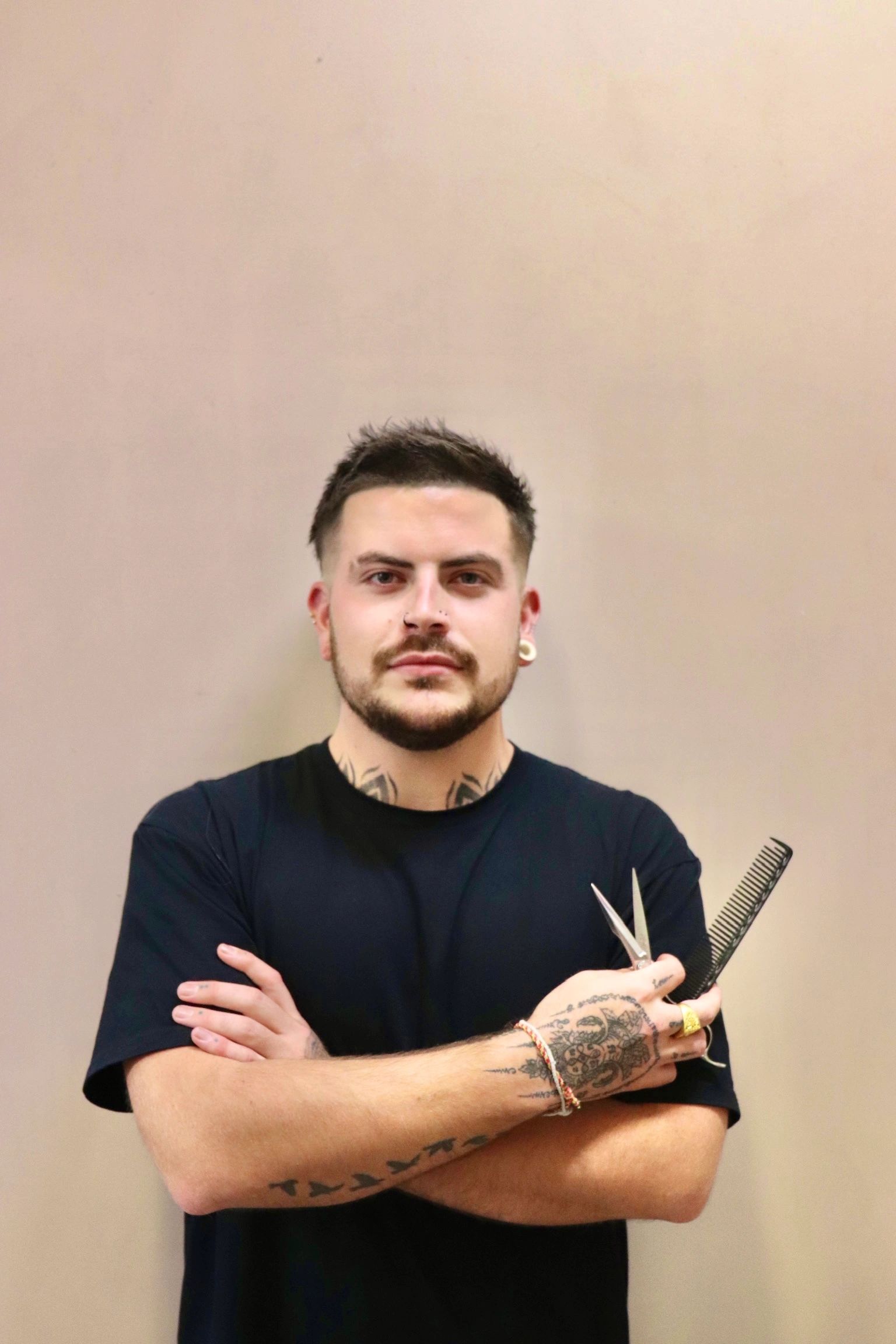 Man with tattoos holding scissors and comb.