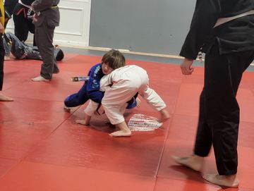 Two kids practicing judo on a red mat.