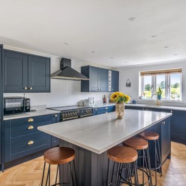 Modern kitchen with navy cabinets, white countertops, and wooden stools around a central island.