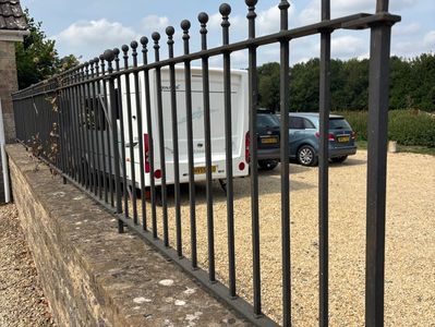 Black metal fence on a stone wall with parked cars and a caravan behind it.