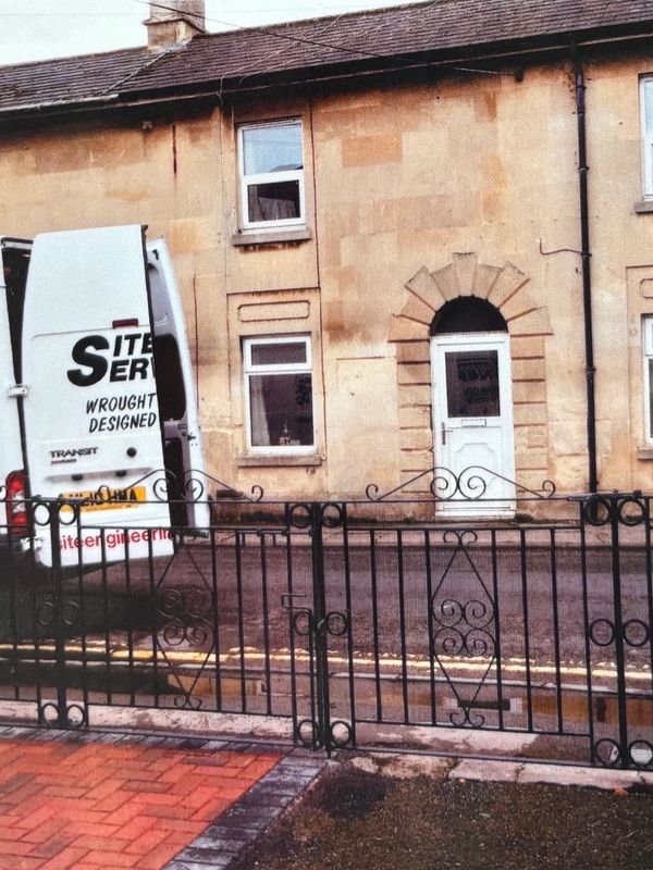 A white service van is parked outside a beige stone house with a decorative black metal fence.
