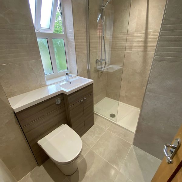 Bathroom setting; picturing a toilet, sink an shower, with beige tiles