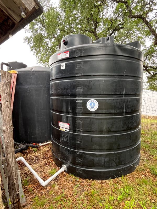 Two large black water storage tanks outside under a tree.