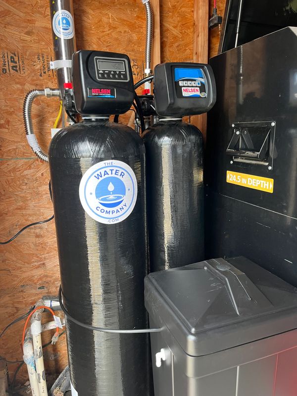 Two black water filtration tanks by The Water Company in a utility room.