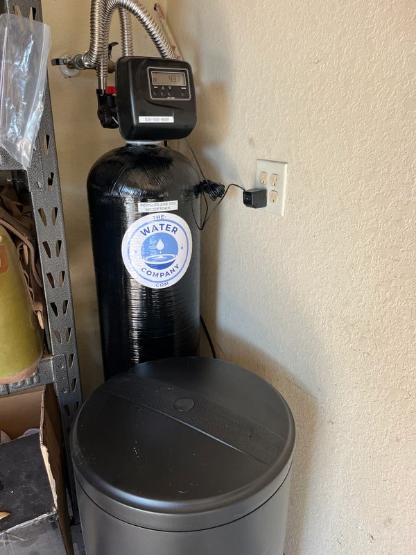 A black water softener tank with a digital control panel installed in a corner.