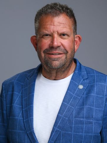Man in blue checkered blazer and white shirt smiling at camera.