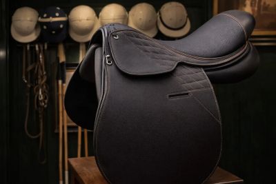 Close-up of a black horse saddle with riding helmets in the background.