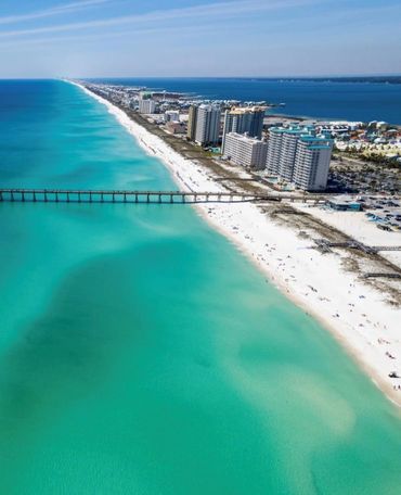 Aerial view of a long beach with turquoise waters and beachfront buildings.