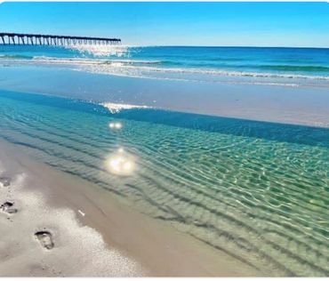 Clear ocean water sparkling under the sun with a pier in the distance.