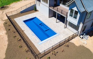 A modern house with a rectangular swimming pool and a fenced yard.