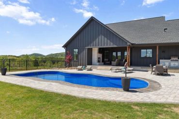 Modern house with a backyard pool and outdoor seating under a clear sky.