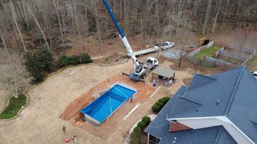 Crane lowering a blue pool into a backyard under construction.