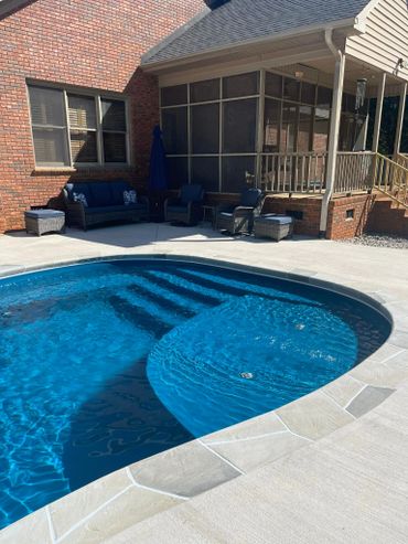 Backyard pool with blue water and patio furniture by a brick house.