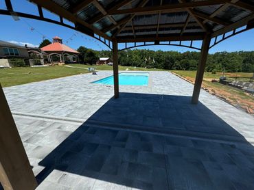 Backyard pool and gazebo with stone patio on a sunny day.