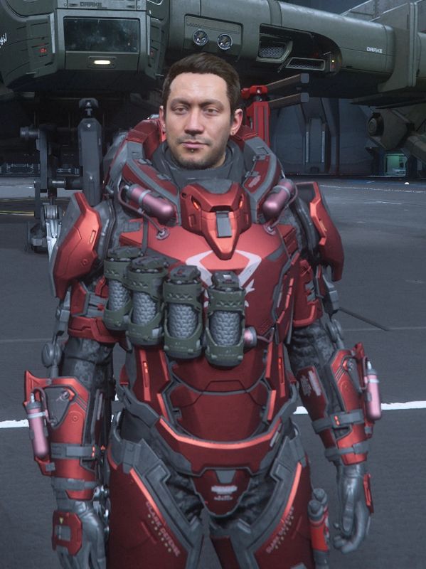 Man in futuristic red armored suit standing in a sci-fi hangar.